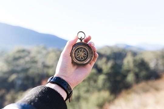 A hand holding up a black and gold compass against a mountain view