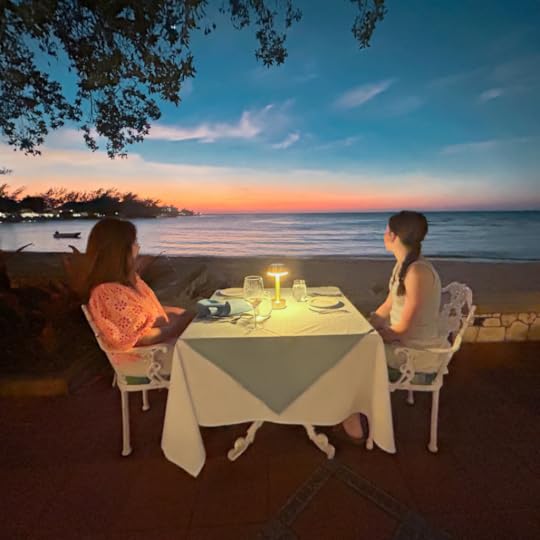 Amy Julia and Marilee sit at a linen-covered table on the beach and look out at the sunset over the ocean