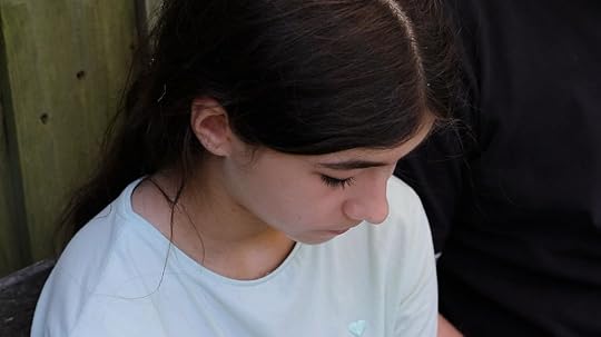 A young girl around 13 sits against a wooden fence with her head down