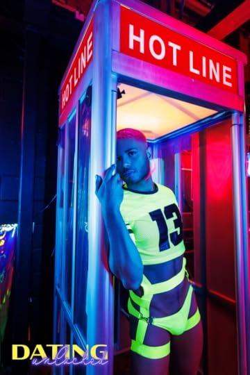 A man with pink hair stands in a phone booth wearing a crop top and neon jockstrap