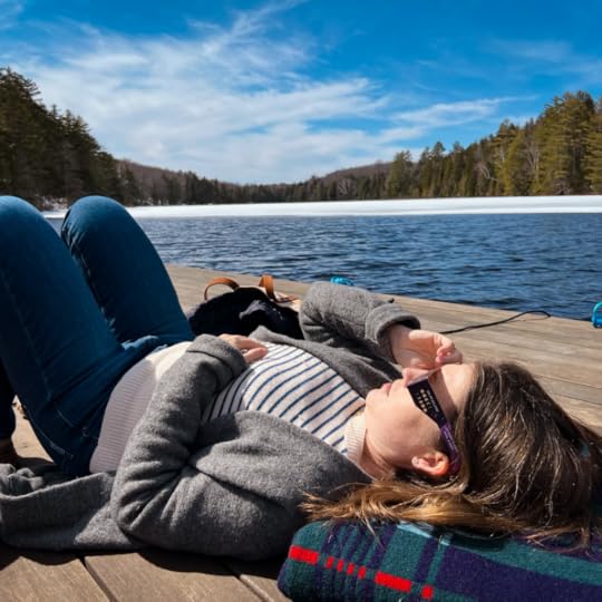 Amy Julie lays on her back on a dock and looks up at the sky. She is wearing eclipse glasses