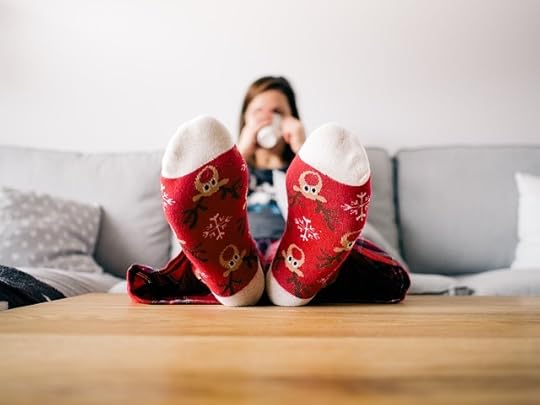 Closeup of cute moose socks on red background attached to a woman out of focus on a couch drinking from a mug.