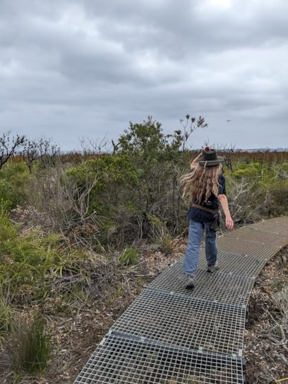 Walking along a path in a swampy, scrubby area, with a seaplane barely visible in the distance