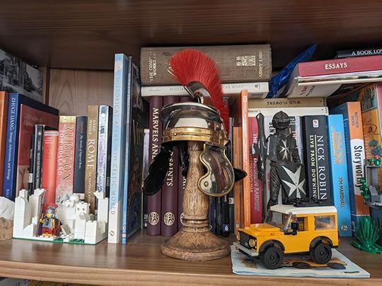 A comically small Roman legionary helmet on a bookshelf.