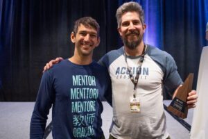A gym owner holds a trophy and smiles beside a Two-Brain mentor.