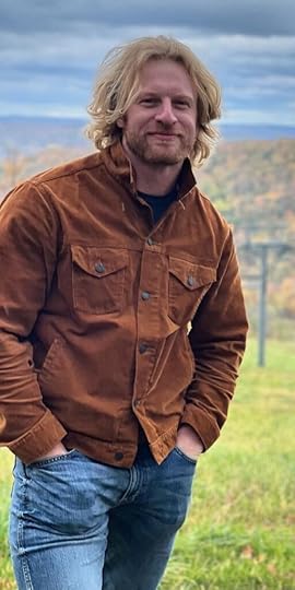 Man with beard standing and wearing jeans and a brown coat