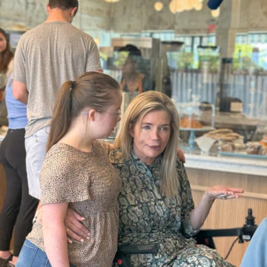 Penny stands next to Katherine Wolf, who is using a wheelchair. They are being interviewed inside Mend Coffee and Goods