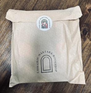 a brown paper bag sealed with a sticker featuring the Maktaba arch logo