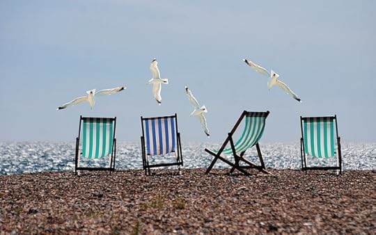4 stiriped canves chairs, in blue and gree, on a beach, with seagulls flying low overhead.