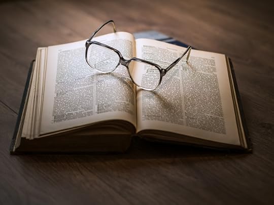 Open textbook with a pair of reading glasses on top of it, set on a wooden table.