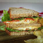 halves of BLT egg sandwich stacked on a board with chips in the foreground.