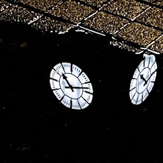 Uhren am Turm des Hauptbahnhofs spiegeln sich in einer abendlichen Pfütze auf dem Bahnhofsvorplatz. ein sehr dunkles Bild