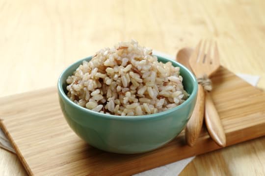 Wooden cutting board with two wooden spoons and a teal bowl with cooked brown rice