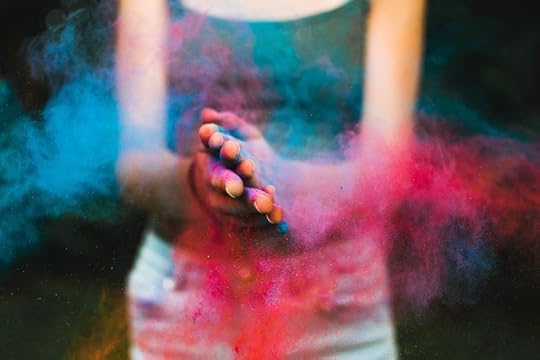 woman in a dark tank top and light jeans calpping blue and red powder in her hands, that creates clouds around her.