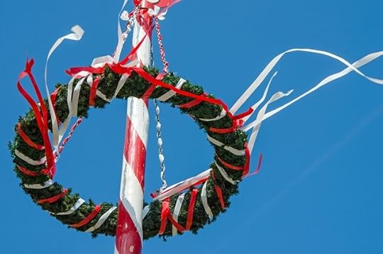Maypole with red and white ribbons streaming down the pole and also around the green wreath at the top of the pole.