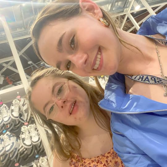 Penny and a friend smiling for a selfie in front of rows of shoes