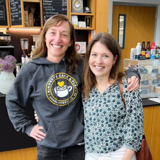 Katie Kishore and Amy Julia stand in Kindness Cafe with their arms around each other and smile at the camera