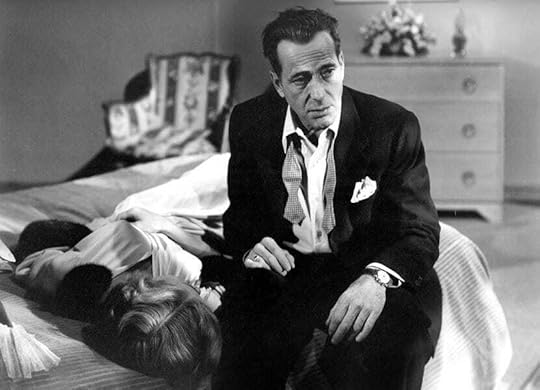 Humphrey Bogart sits on a bed next to the prone Gloria Grahame in