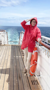 Laughing woman in red windbreaker clings to rail on the windy deck of a ship