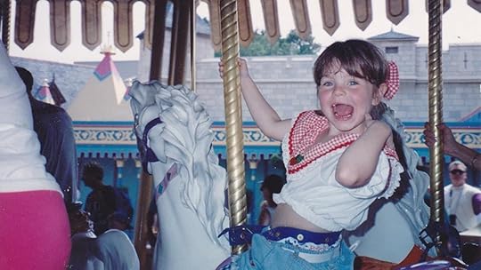 A young toothlee girl smiles sitting atop a horse on a carousel