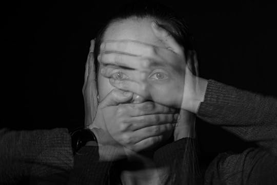 Image: a double-exposed photograph of a woman's face with, in the multiple exposures, her hands covering her ears, eyes, and mouth.