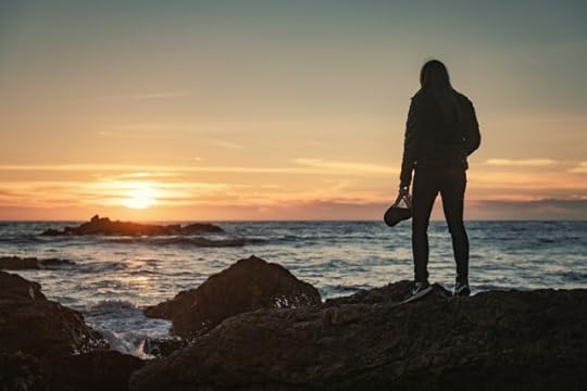 person standing on rocks beside the sea watching the sunset. be here now and mindfulness in motion.