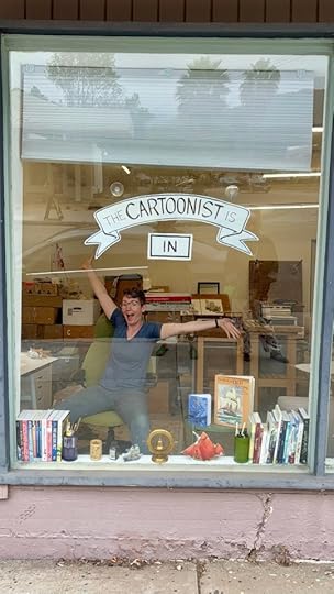 Lucy beaming in a window full of comics and books under a hand-lettered sign reading "the cartoonist is in."