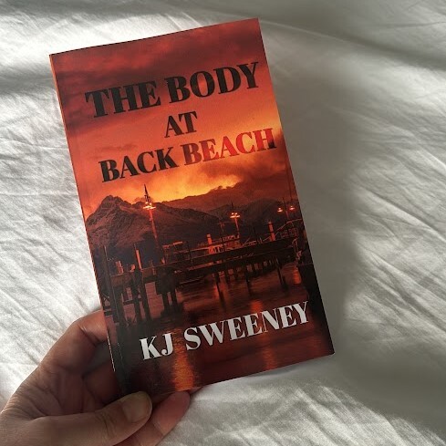 A hand holding a preorder copy of the body at back beach