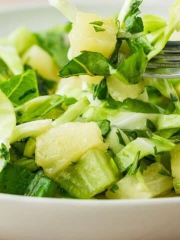 Tasty pineapples, arugula and cabbage with a dressing on a fork close up.