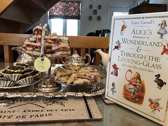 Lewis Carroll's Alice's Adventures in Wonderland & Through the Looking Glass and What Alice Found There, next to a display of tiny sandwiches, mini tarts, and scones. There's a silver sugar bowl and the edge of a teapot in the background. A little label that says 