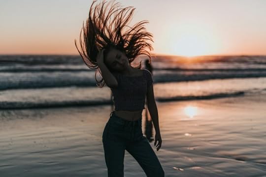 Woman flipping her hair at sunset beside the ocean. Positivity is easier said than done.