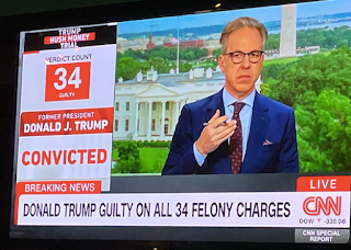 The TV is showing the headline, Donald Trump guild on all 34 felony charges.' There's a male news anchor (Jake Tapper) sitting at the desk, broadcasting. There's a graphic that says it's live on CNN.