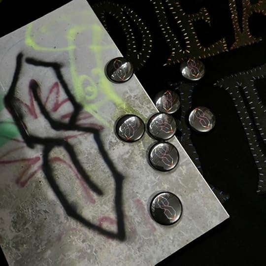 Copy of Cool S covered in a pile of Cool S badges. The book cover and badges have a cool S on each of them. The book cover is spray painted black on grey concrete, the badges are rainbow on a black background.