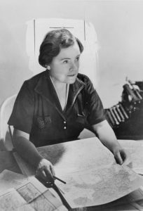 Black and white photo of Anne O'Hare McCormick seating at a table, which is covered with maps