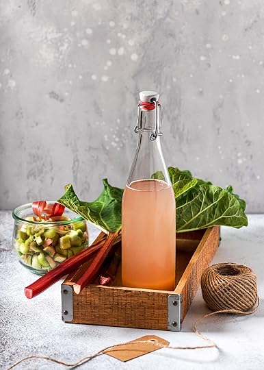 A bottle of rhubarb syrup with rhubarb stalks in a wooden box.