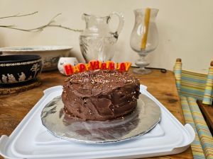 A picture of a cake covered in chocolate icing with an orange and red ‘happy birthday’ candle on top