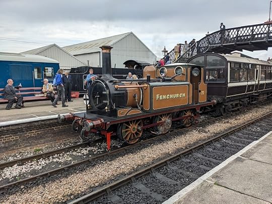 'Fenchurch', a small golden-brown steam locomotive, waiting at its platform with carriages in tow.