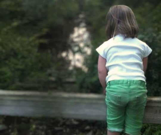 photo of Penny when she was five years old. She is standing on a wooden railing, with her back to the camera, and looking at a blurred creek below