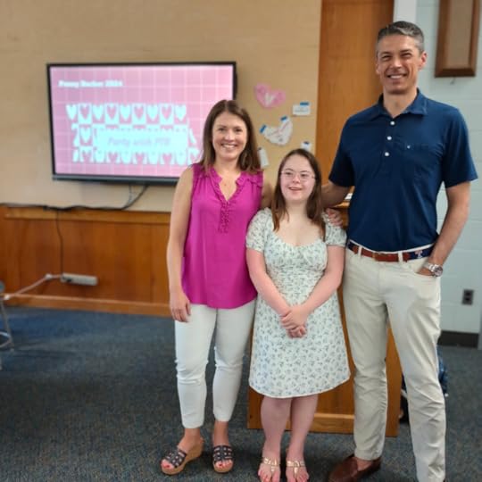 Amy Julia, Penny, and Peter smile for the camera in a classroom. On a TV screen behind them is a pink background and text that says: Party with PTB