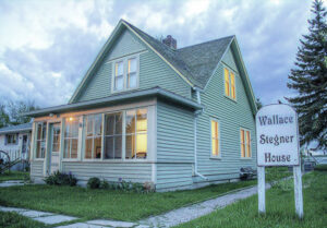 Traditional two-story house with four gables, enclosed front porch, covered with clapboard siding painted light green, surrounded by green grass