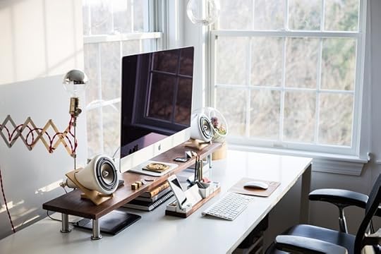 Home office desk with window overlooking garden. Desk is neat, with computer mointor and keyboard, speakers, and phone in a holder, rest of desk clear.