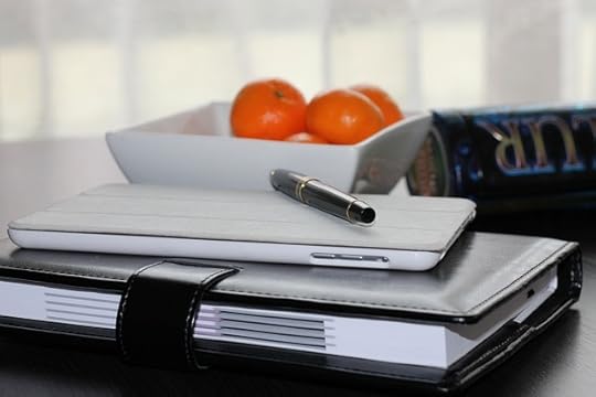 square white bowl of oranges behind a stacked datebook and cell phone, with a pen on top.