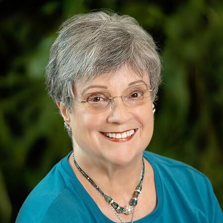 A smiling woman with a bright blue top and eyeglasses faces you.