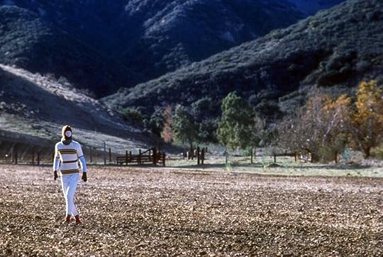 A masked, white-clad figure walks through a barren field in Todd Haynes'