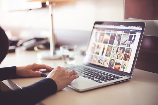 Hands typing on a laptop with an array of thumbnail images on the screen.