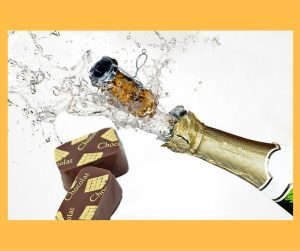 a bottle of champagne with the cork flying out over several pieces of chocolate 