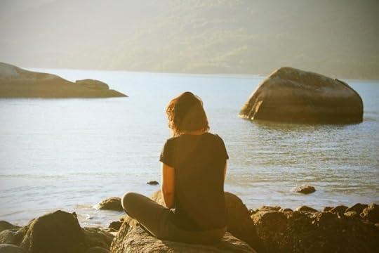 A woman seated on a rock alongside a bay, focusing within