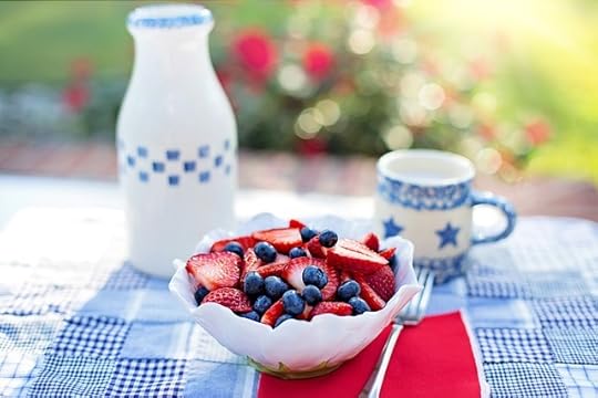 Strwaberries and blueberryies in a white bowl on a blue and white checked tablecloth, with blue and white mug behnd it.