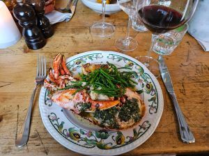 A plate on a table with lobster and samphire with a glass of wine.