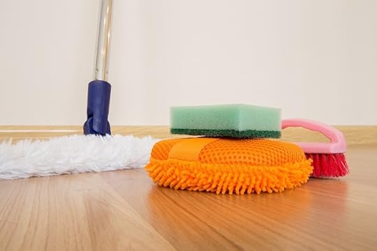 White mop, orange scrubber, green sponge, and pink scrubbing brush on a wooden floor.